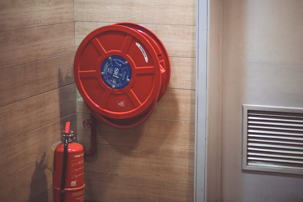 Red fire hose reel and extinguisher inside a building corner.