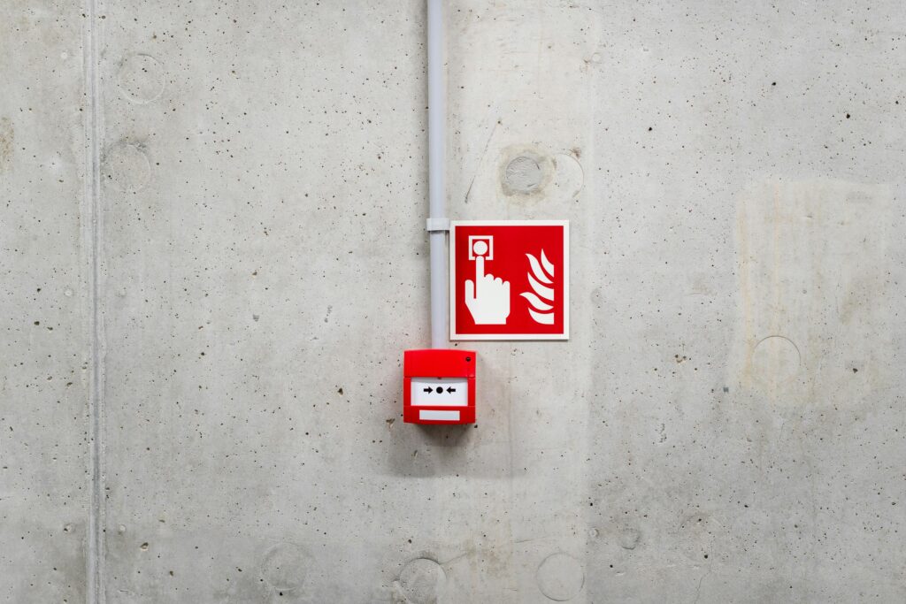 Red emergency fire alarm on a gray concrete wall in Poznań, enhancing safety awareness.