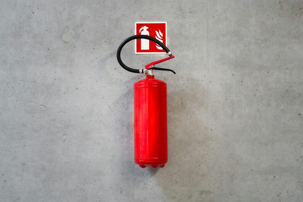 A red fire extinguisher mounted on a concrete wall indoors with emergency signage.