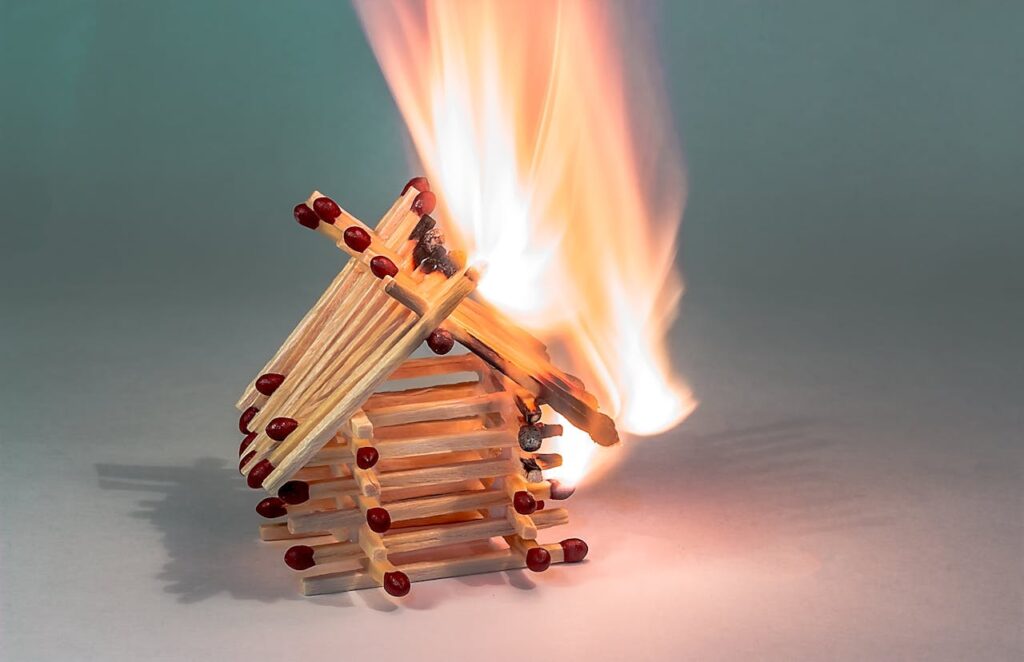 Close-up of a small matchstick house ablaze, showcasing flame and heat.